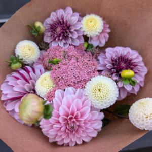 Pink and purple colored flowers arranged in a bouquet wrapped in kraft paper.